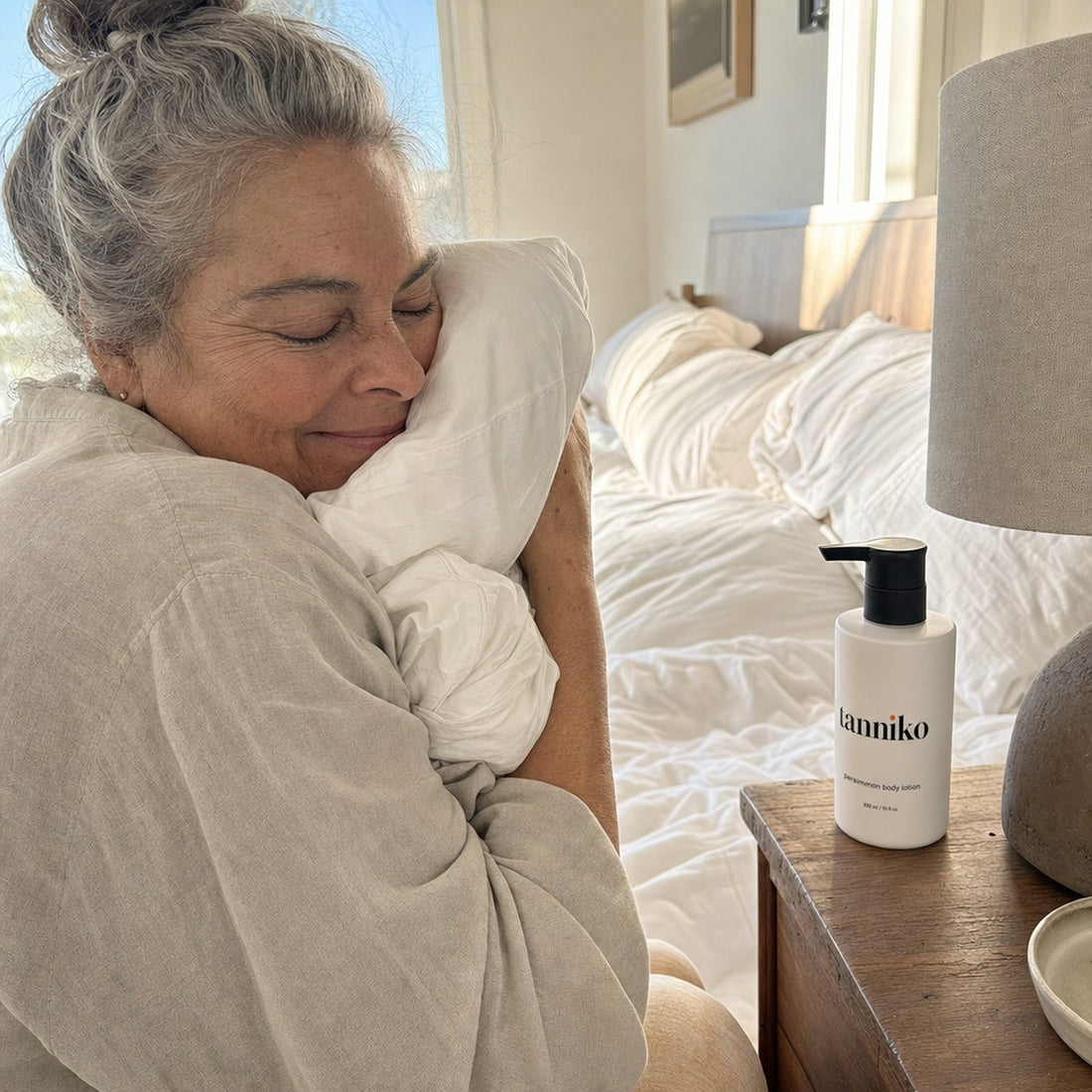Woman holding a fresh pillow, Tanniko persimmon body lotion on the nightstand